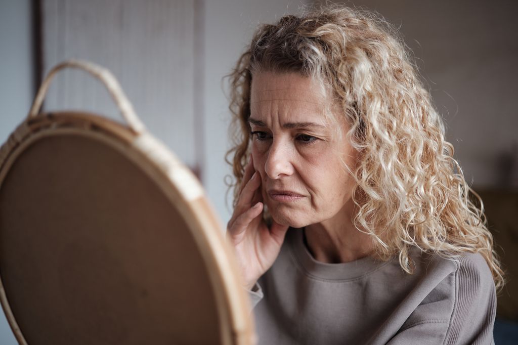 Sad middle-aged woman looking in mirror, 