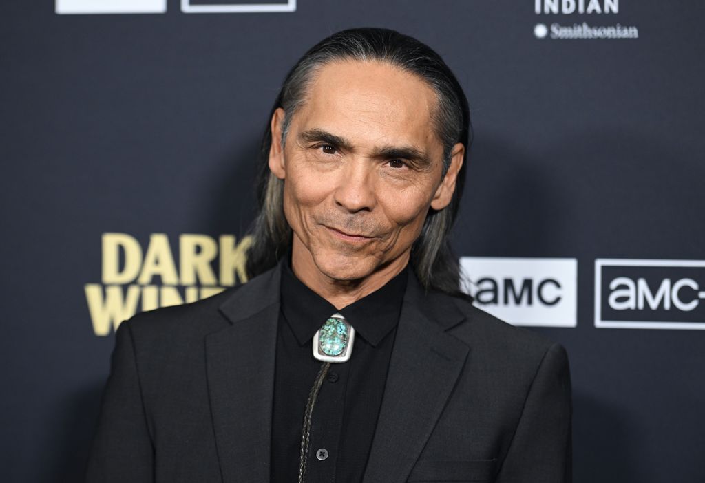 Zahn McClarnon wearing a black suit at the red carpet premiere of Dark Winds season three.