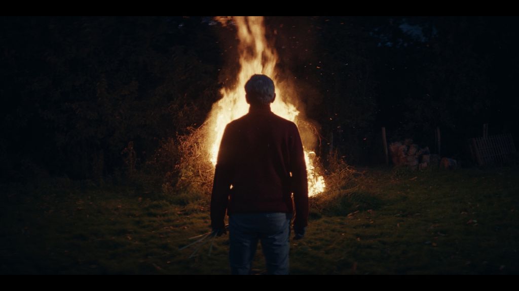 A man standing in front of a bonfire with his back to the camera