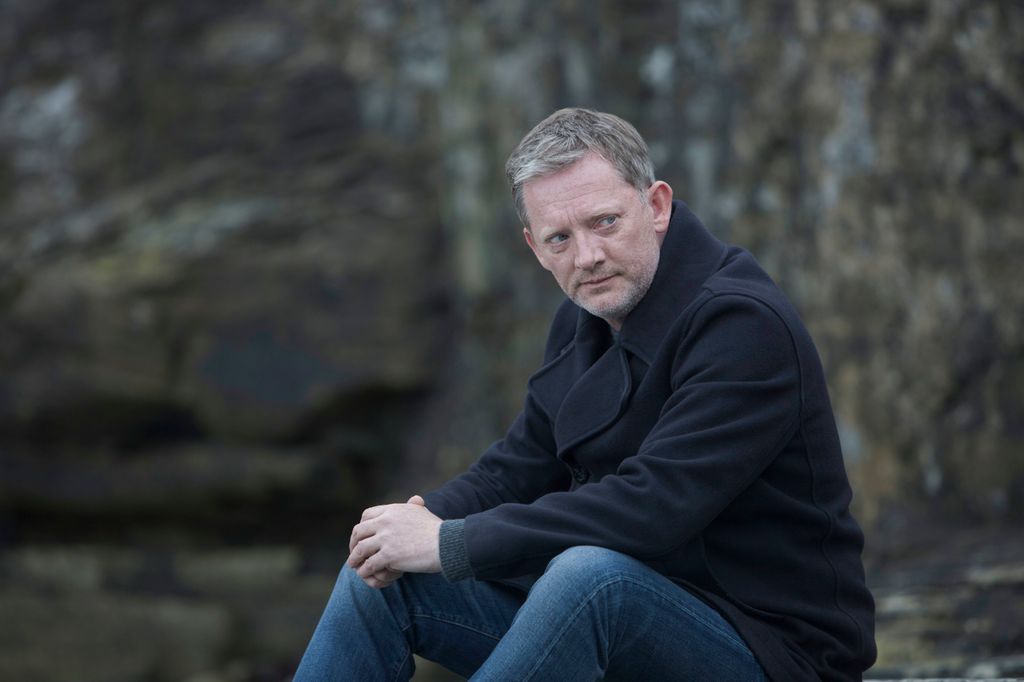 Man with grey hair sitting on rock 