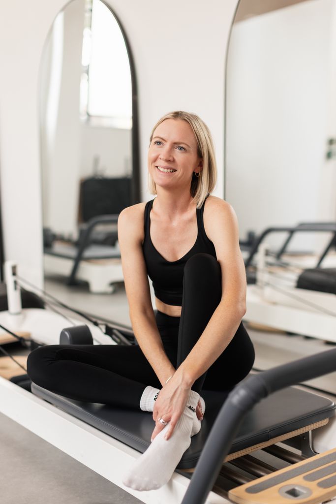 Woman sitting and smiling on a Pilates bed 