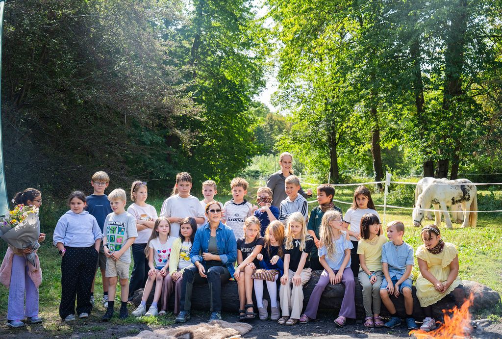 Queen Mary sitting around a campfire with schoolchildren