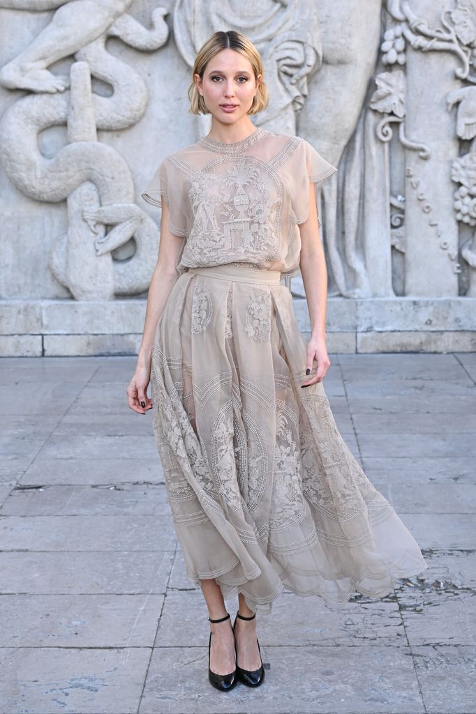 Maria Olympia of Greece wearing a long embroidered white dress and black heels 