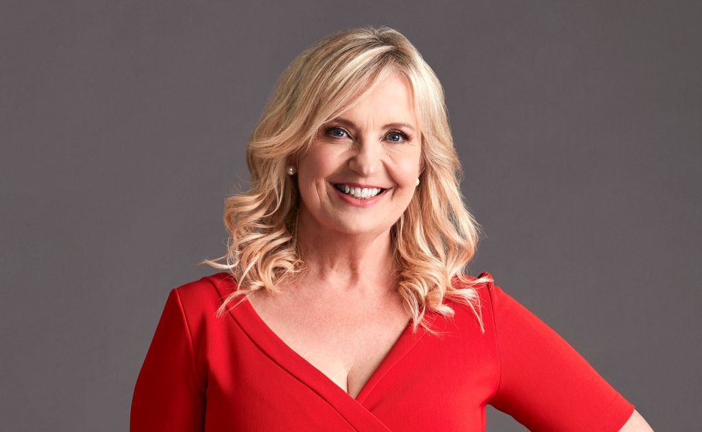 Carol Kirkwood smiling while wearing a red short-sleeved dress with her blonde hair worn loose