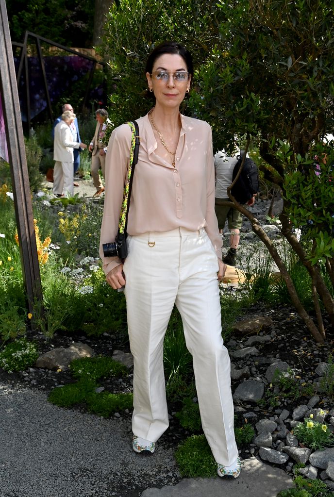 Mary McCartney wears a blush blouse, white trousers and floral trainers with glasses and a camera at Chelsea Flower Show.