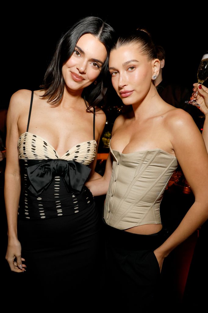 Kendall Jenner and Hailey Bieber  pose for the camera, Hailey wears a beige corset top and Kendall wears a polka dot strappy top with bow detail