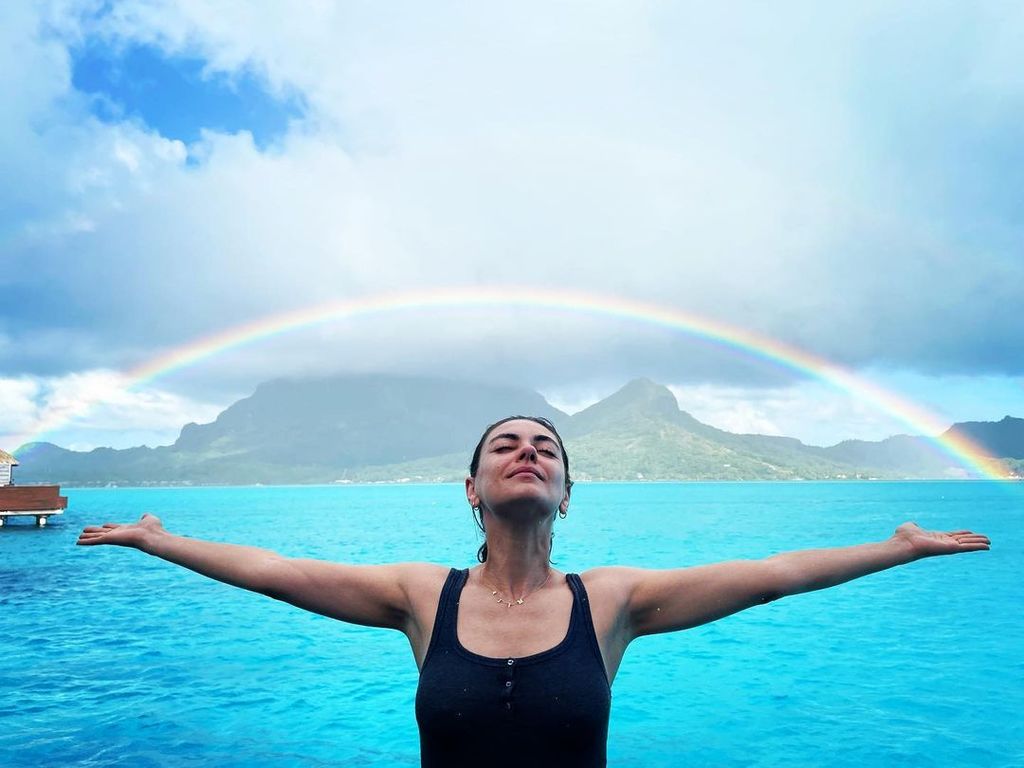 Mila Kunis smiling under a rainbow