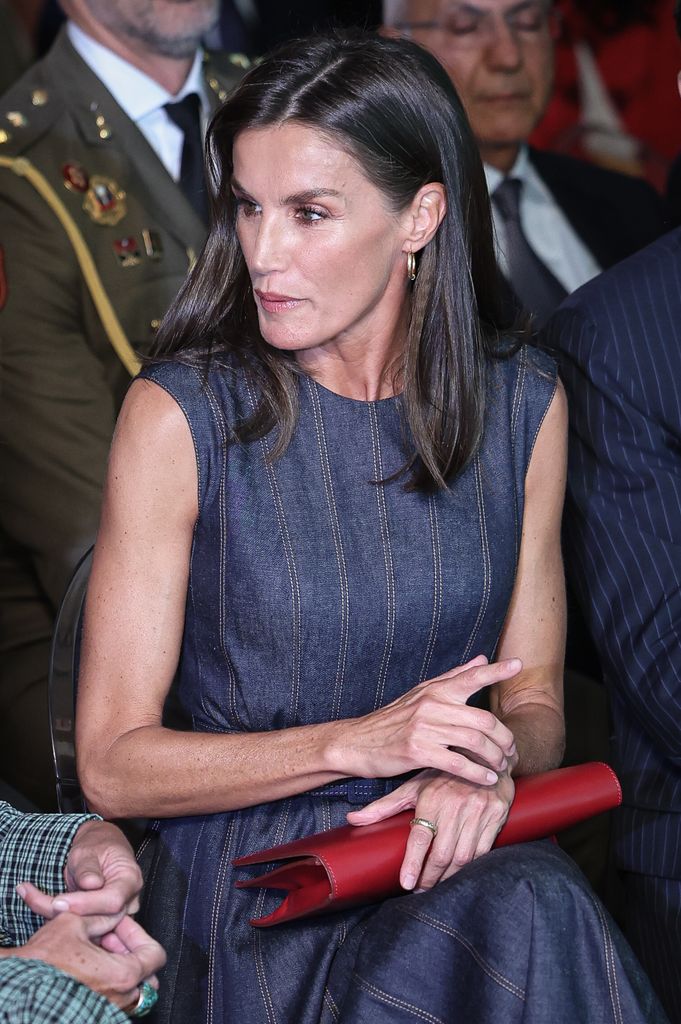 Queen Letizia sitting in denim dress with red clutch