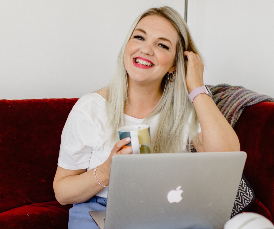 Blonde woman smiling while on her laptop drinking from a mug