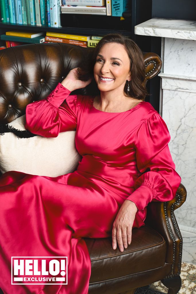 shirley ballas in a cerise pink dress reclining on a chair 