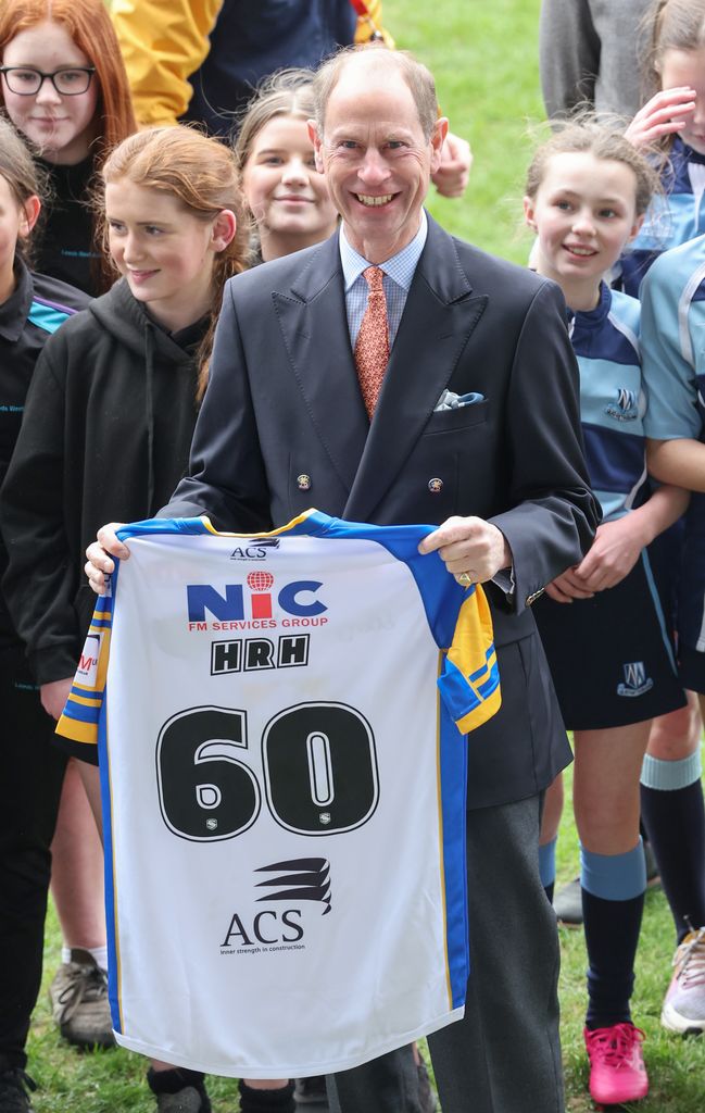 Prince Edward holding a rugby jersey in front of a group of young girl