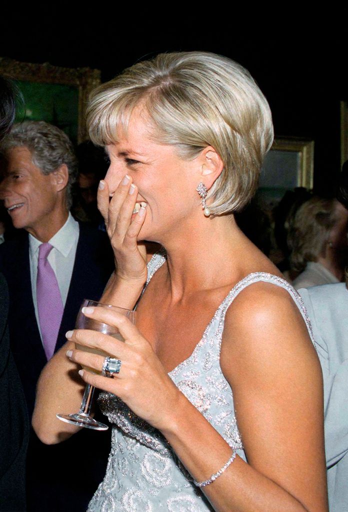 Diana, Princess Of Wales tertawa dengan tangan menutupi mulut dan tangan memegang gelas anggur