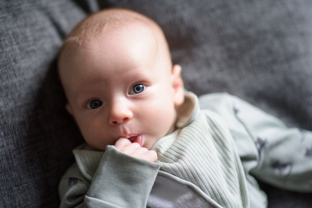 Image of a newborn baby teething laying on his back with finger in his mouth.