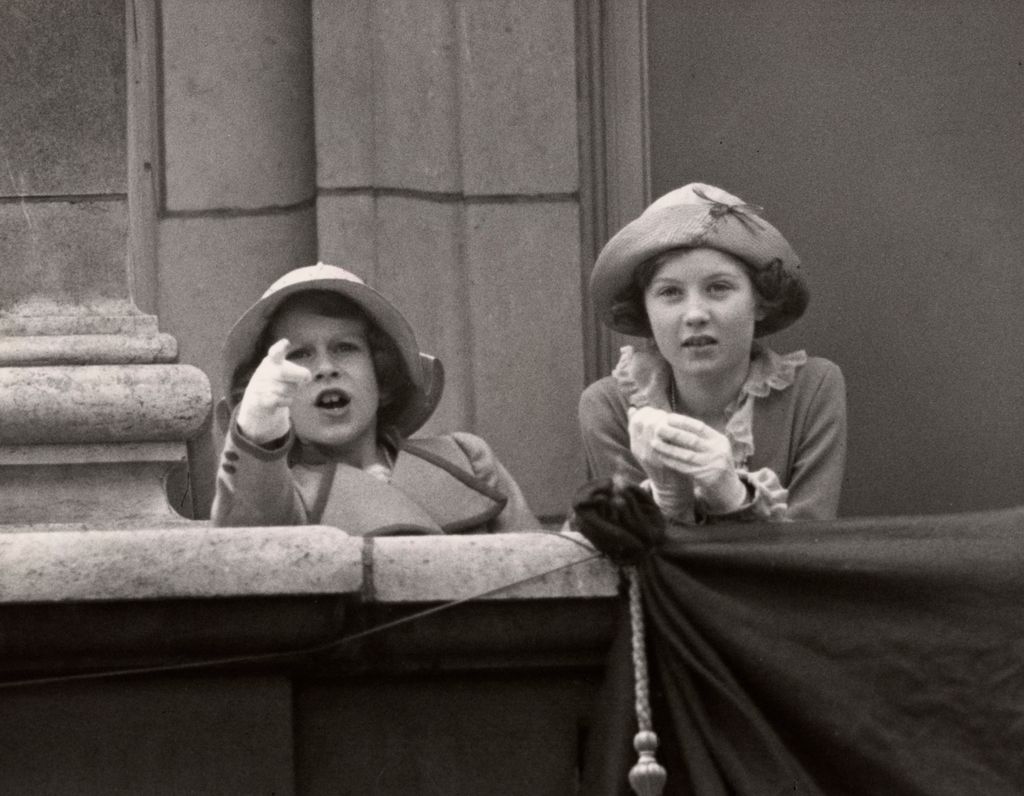 Black-and-white photo of a young Queen and girl pointing out over Buckingham Palace