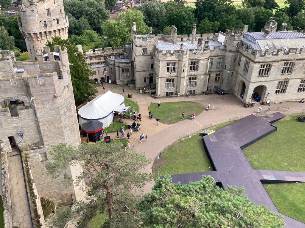 Warwick Castle courtyard from above with people wandering around path and trees in the distance