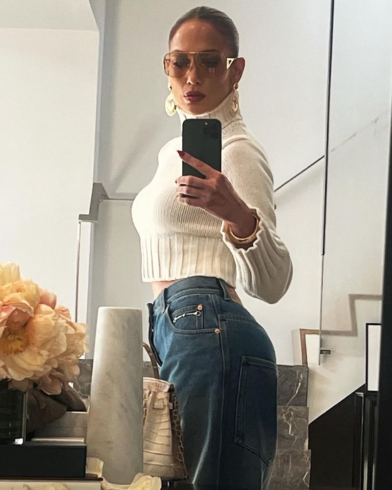 Jennifer Lopez poses in a cream sweater and denim pants