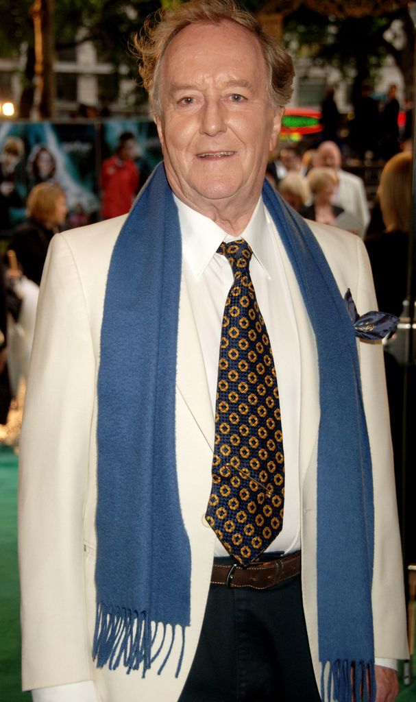 Robert Hardy in a white suit and blue scraf