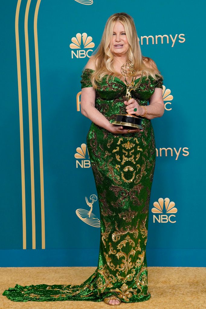 Jennifer Coolidge wears an odd the shoulder full length green and gold dress with train detail