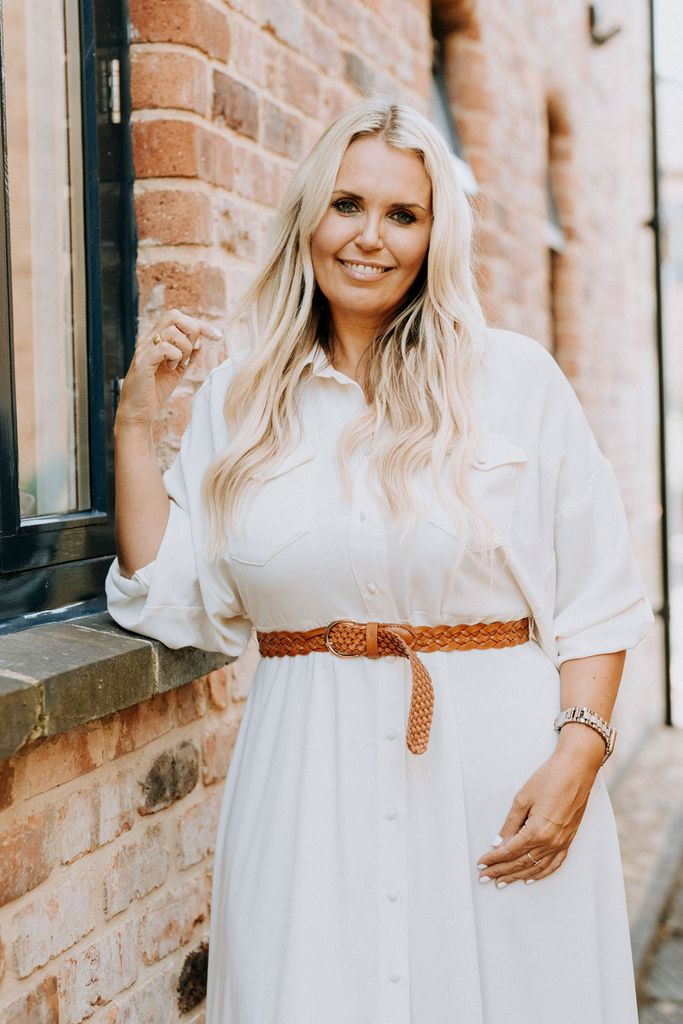 woman smiling in a white dress with a brown belt