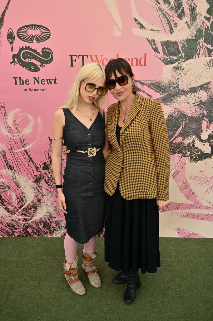 Betty Goffey and Pearl Lowe pose together, one in a gingham blazer and one in a sleeveless charcoal dress with pink tights and slouchy boots at FT Weekend x The Newt party at the Chelsea Flower Show