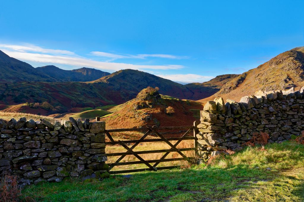 A view of a traditional dry stone wall and wooden gate in the hilly landscape of the English Lake District