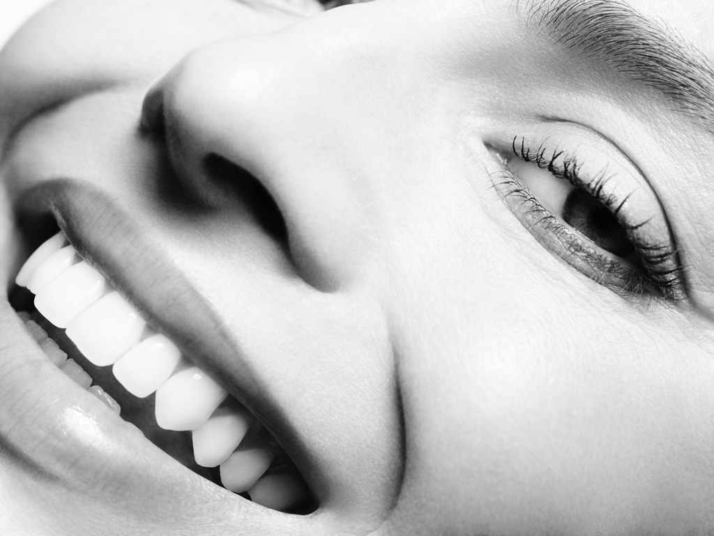 This black-and-white close-up of Margot Robbie from Chanel focuses on her radiant smile and facial details. The image highlights her flawless teeth, smooth skin, and naturally beautiful eyelashes, capturing an intimate and joyful expression. The composition is elegant and minimal, emphasizing purity and the essence of timeless beauty.