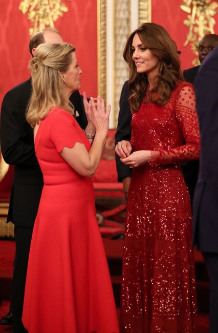 sophie and kate stand speaking in long red dresses