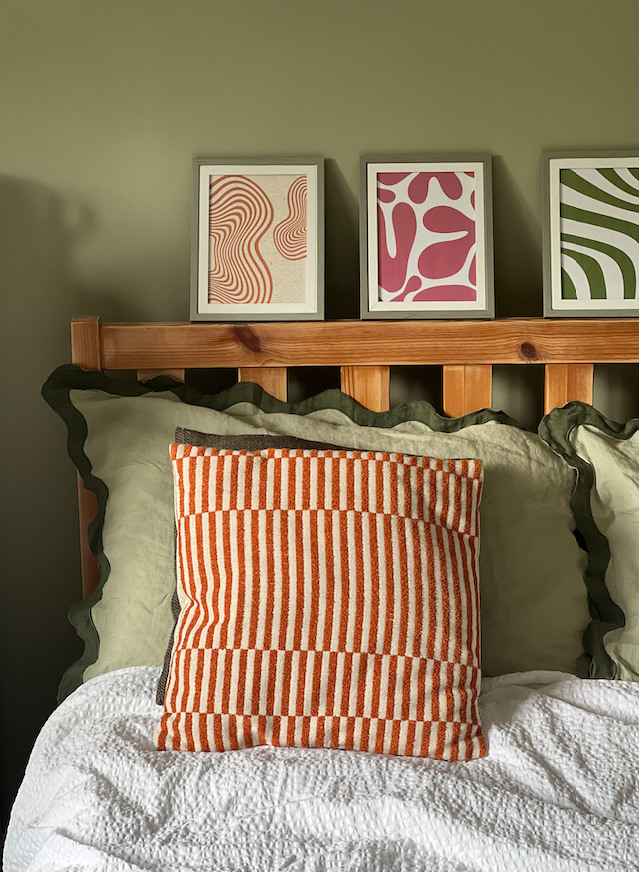 bed with orange cushion and colourful artworks on bed frame