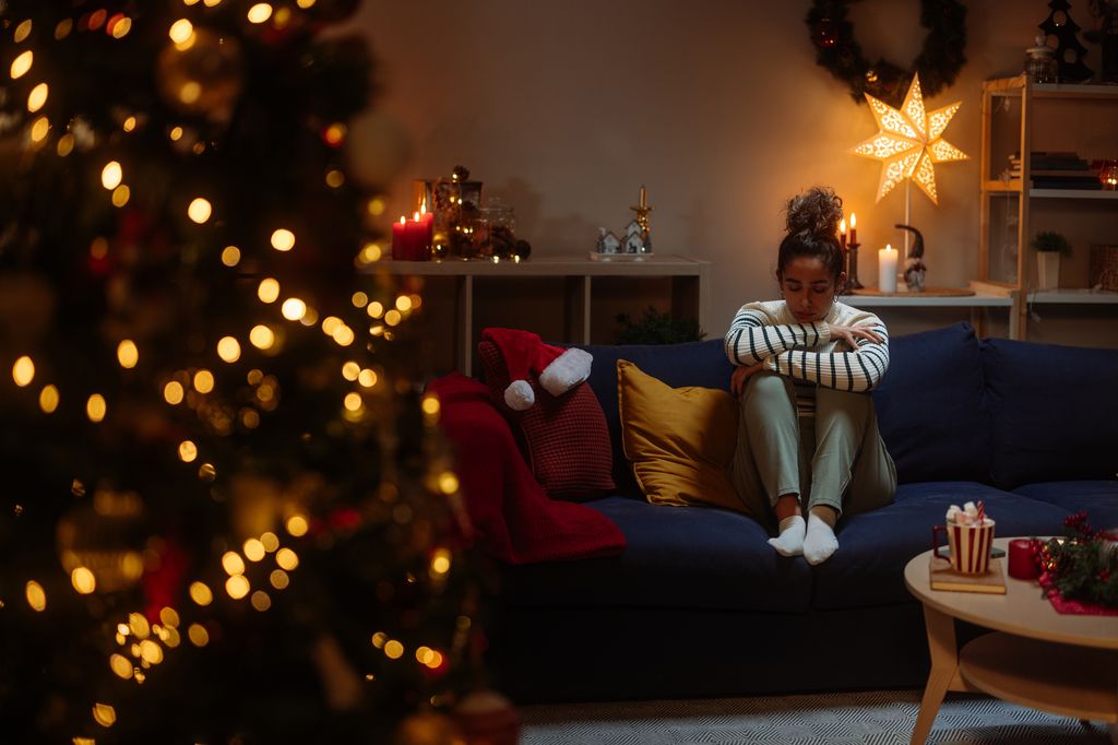 Young woman feeling lonely and depressed during christmas time, sitting on the sofa in a decorated living room