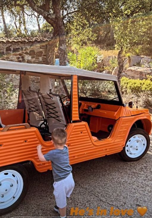A young boy walking towards an orange mini jeep