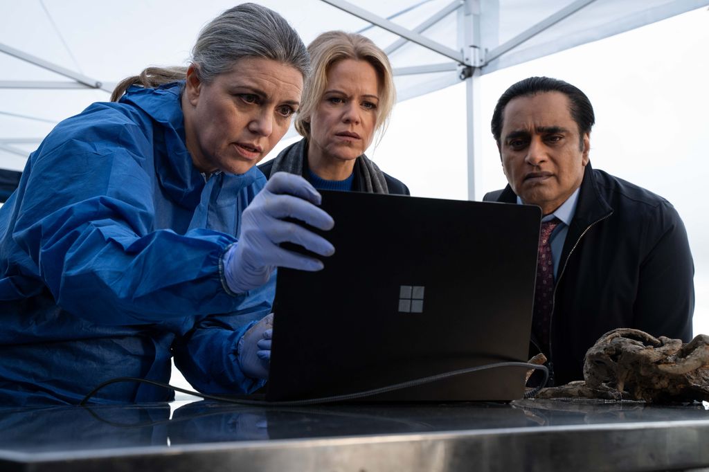 Three people looking at laptop screen, one person in blue hazmat suit