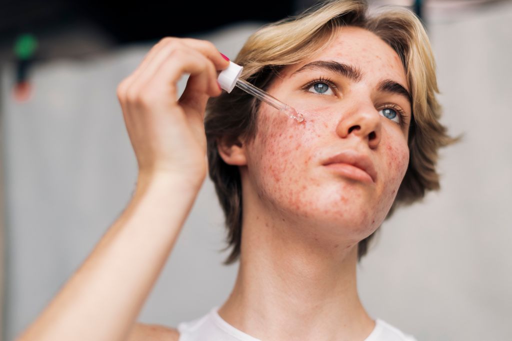 Contemplative young man using face serum against white background