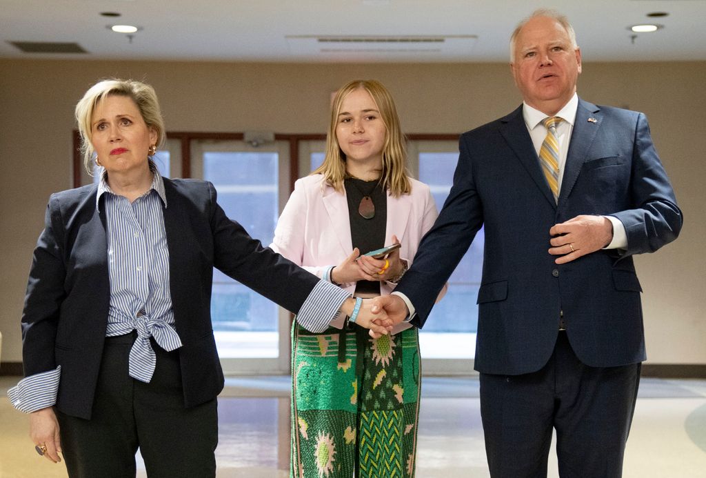 Gwen and Tim Walz hold hands in front of their daughter, Hope, during the 2022 State DFL Convention