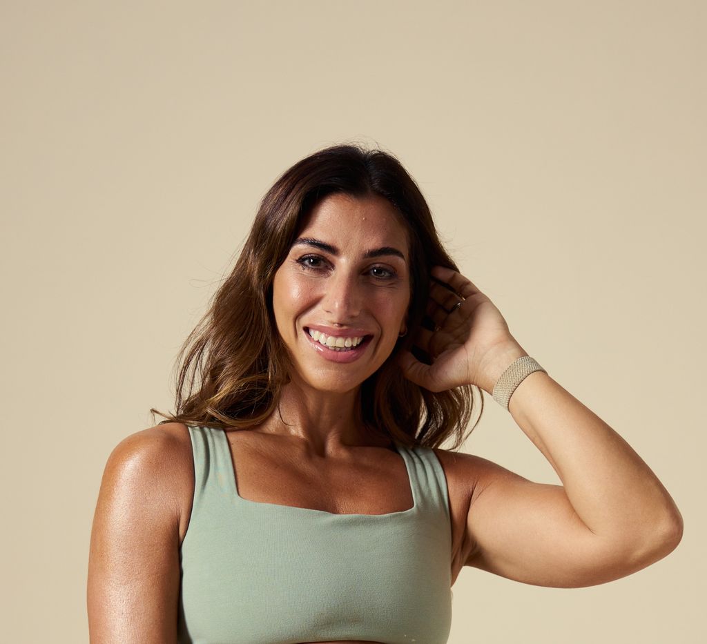 Dark haired woman in an olive green top touching her hair 