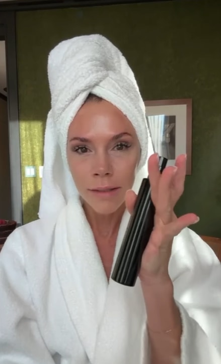 Victoria in robe and towel on head with skincare product in hand