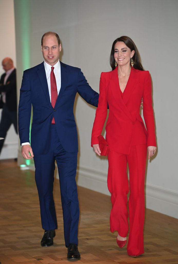 Prince William in suit walking beside Catherine, Princess of Wales in red suit 