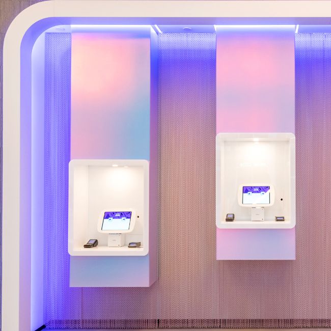 two self checkout points with card readers lit with neon lights and positioned at different heights inside yotel
