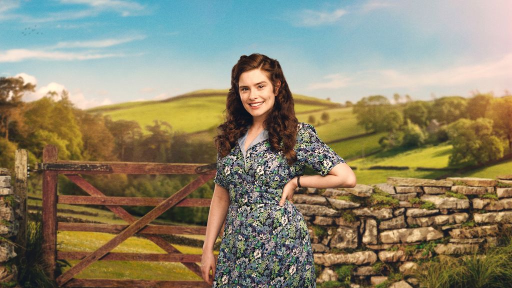 A woman stands in front of a stone wall