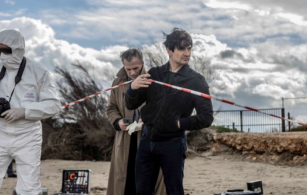 man holding up police tape at crime scene on beach