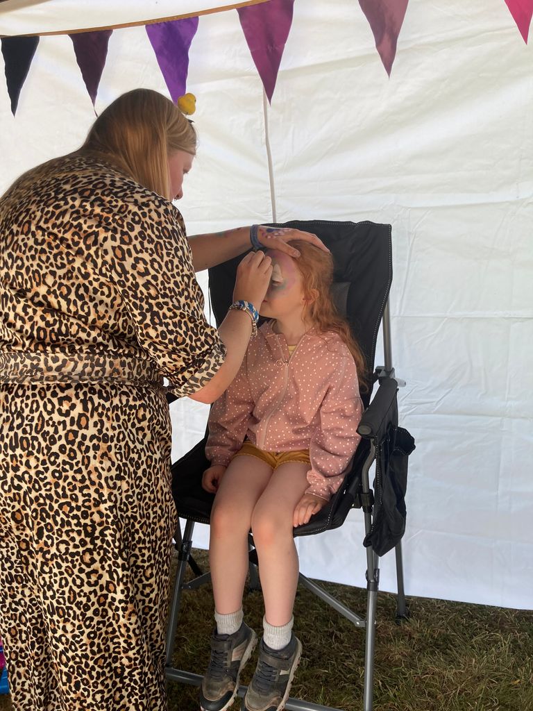 Woman painting a girl's face as she sits down