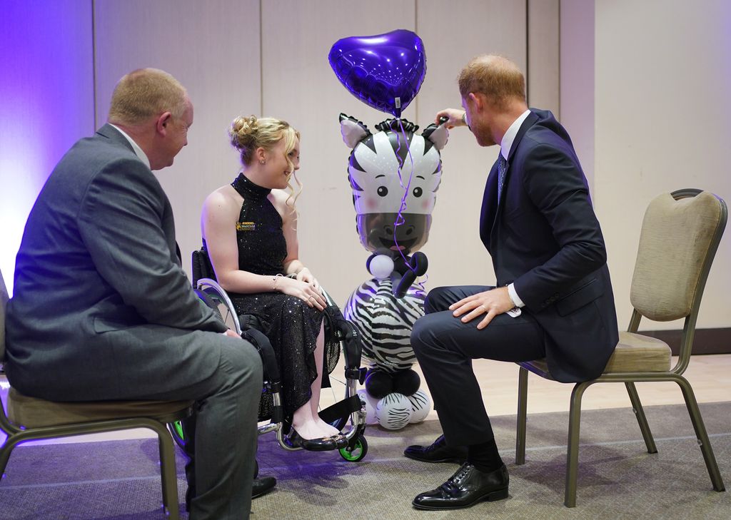 Prince Harry in a suit touching a zebra balloon and making a wellchild guest laugh