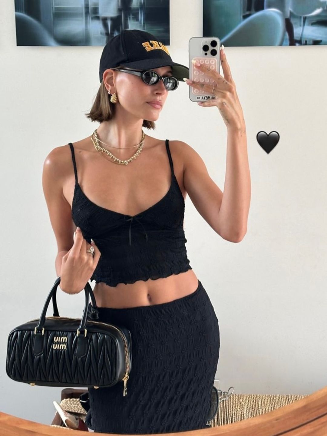 Hailey Bieber taking a mirror selfie holding a black Miu Miu bowling bag 