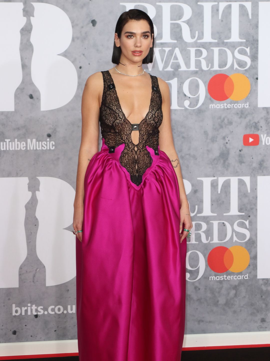 Dua Lipa seen on the red carpet during The BRIT Awards 2019 in a bright pink and black lace gown