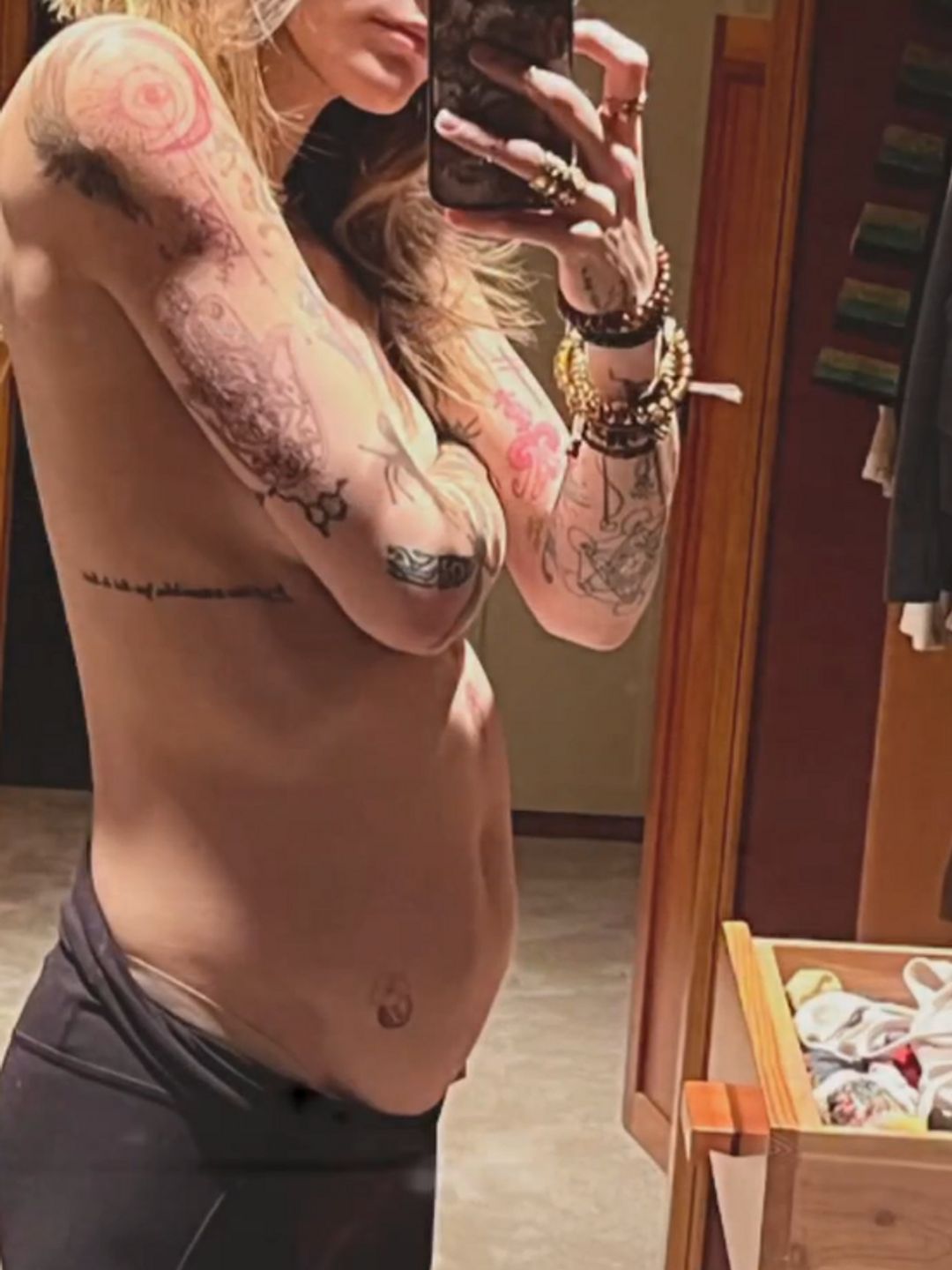 Paris Jackson taking a mirror selfie, her arm covering her naked chest, she is wearing leggings