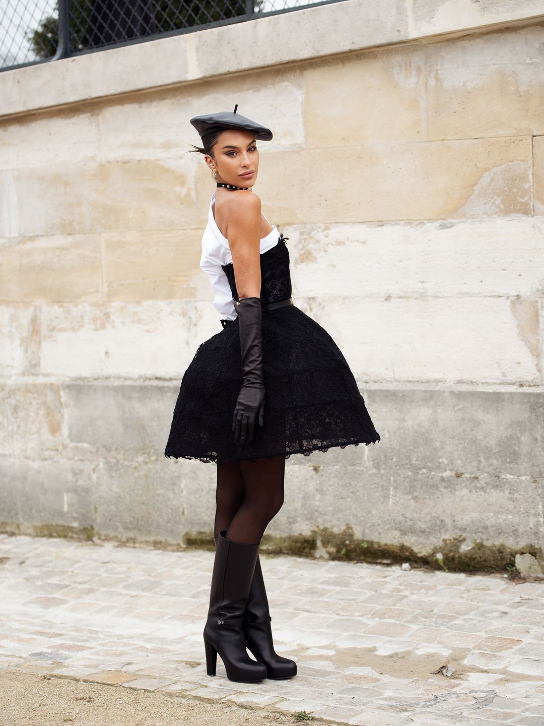 Jessica Aidi wears white one sleeve shirt, black strapless dress in lace, black beret, black leather gloves and black high heel boots outside Dior 