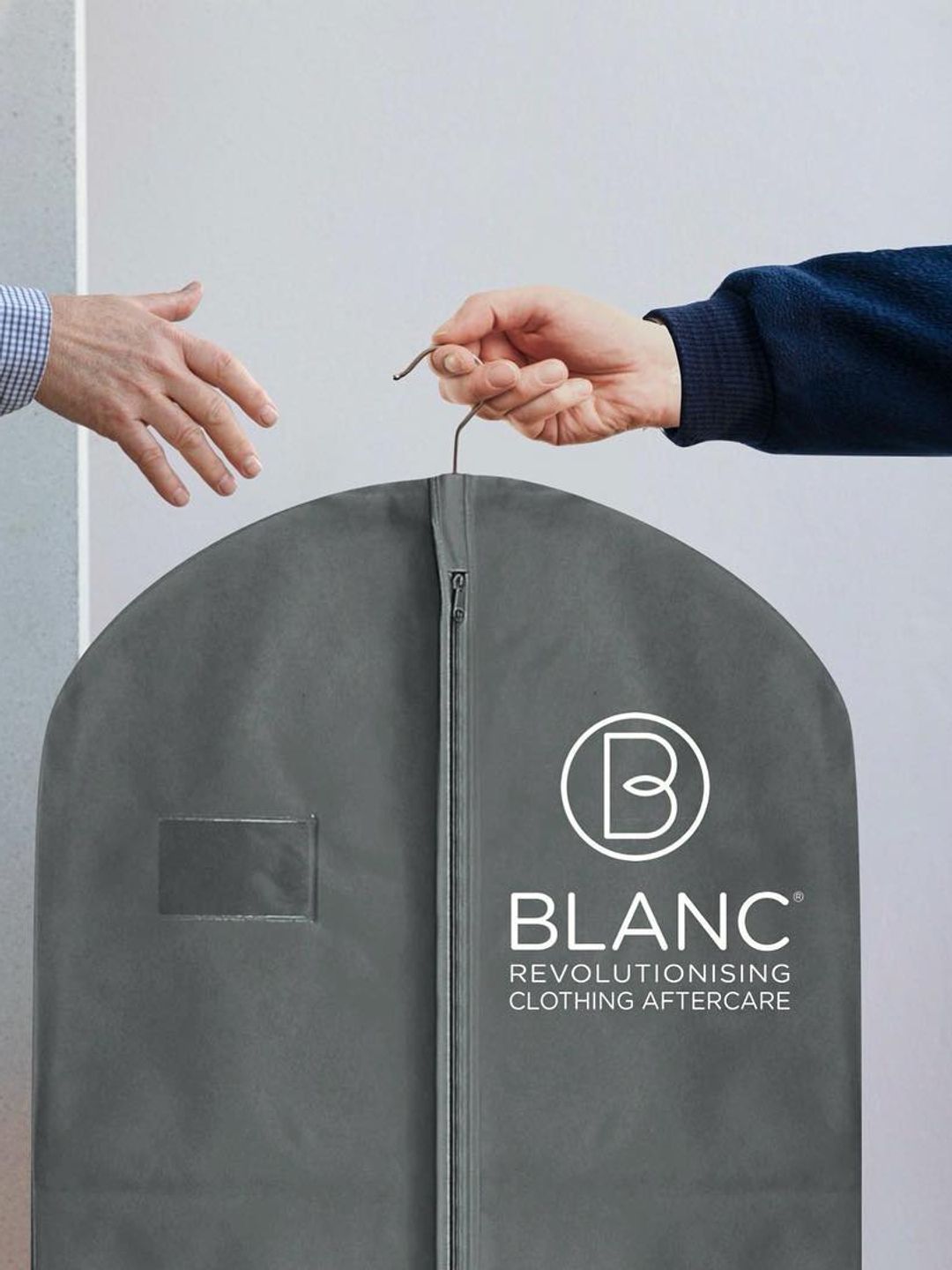 A photo of someone giving someone else a dry cleaning bag filled with clothes