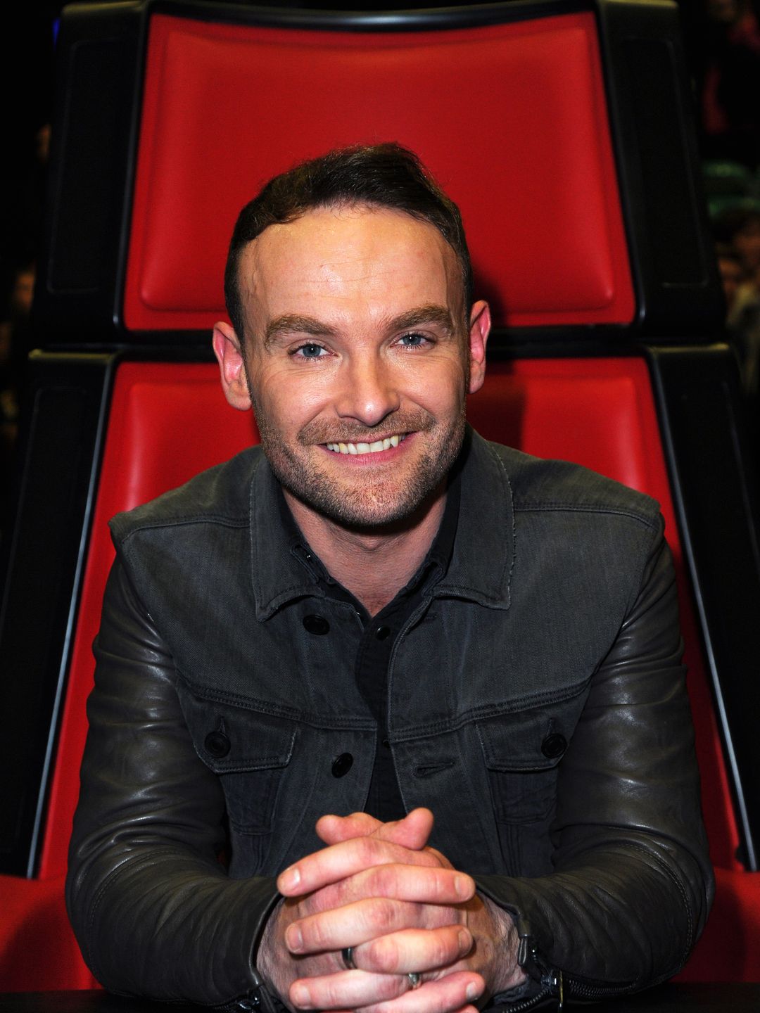 Kevin Simm in a leather jacket sat in a red chair