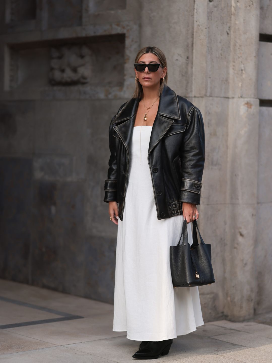 Woman is wearing a white dress with an oversized black leather jacket