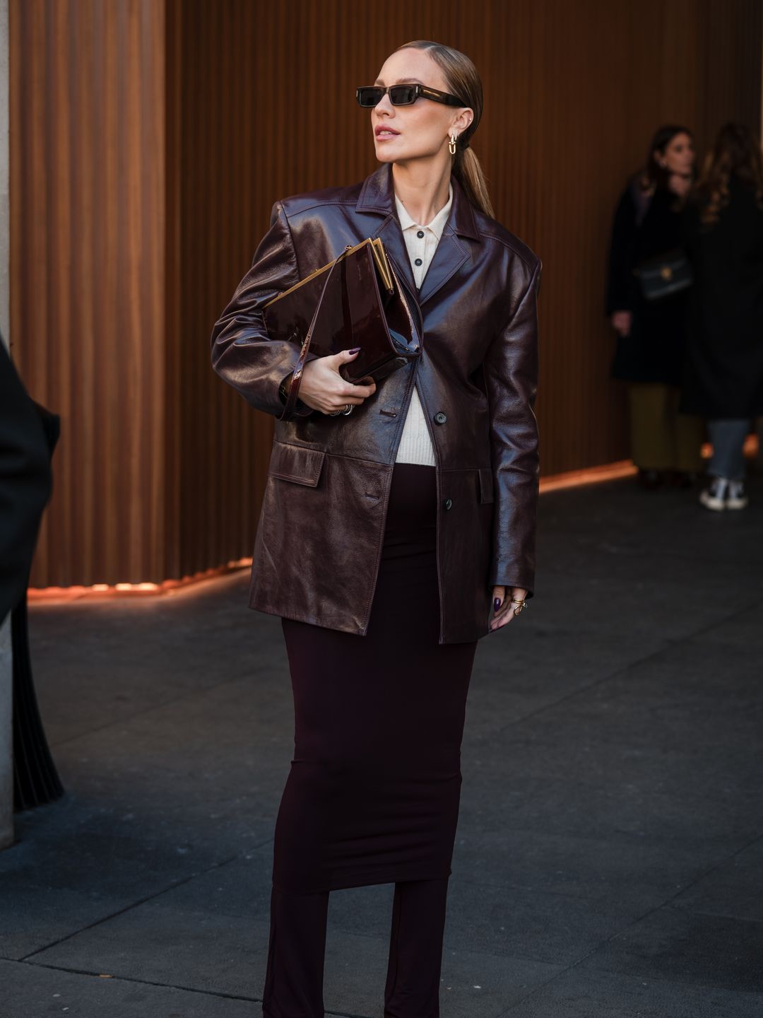 Viky Rader wears beige polo neck , brown leather blazer, brown skirt over pants, black heels with gold details, outside Zimmermann