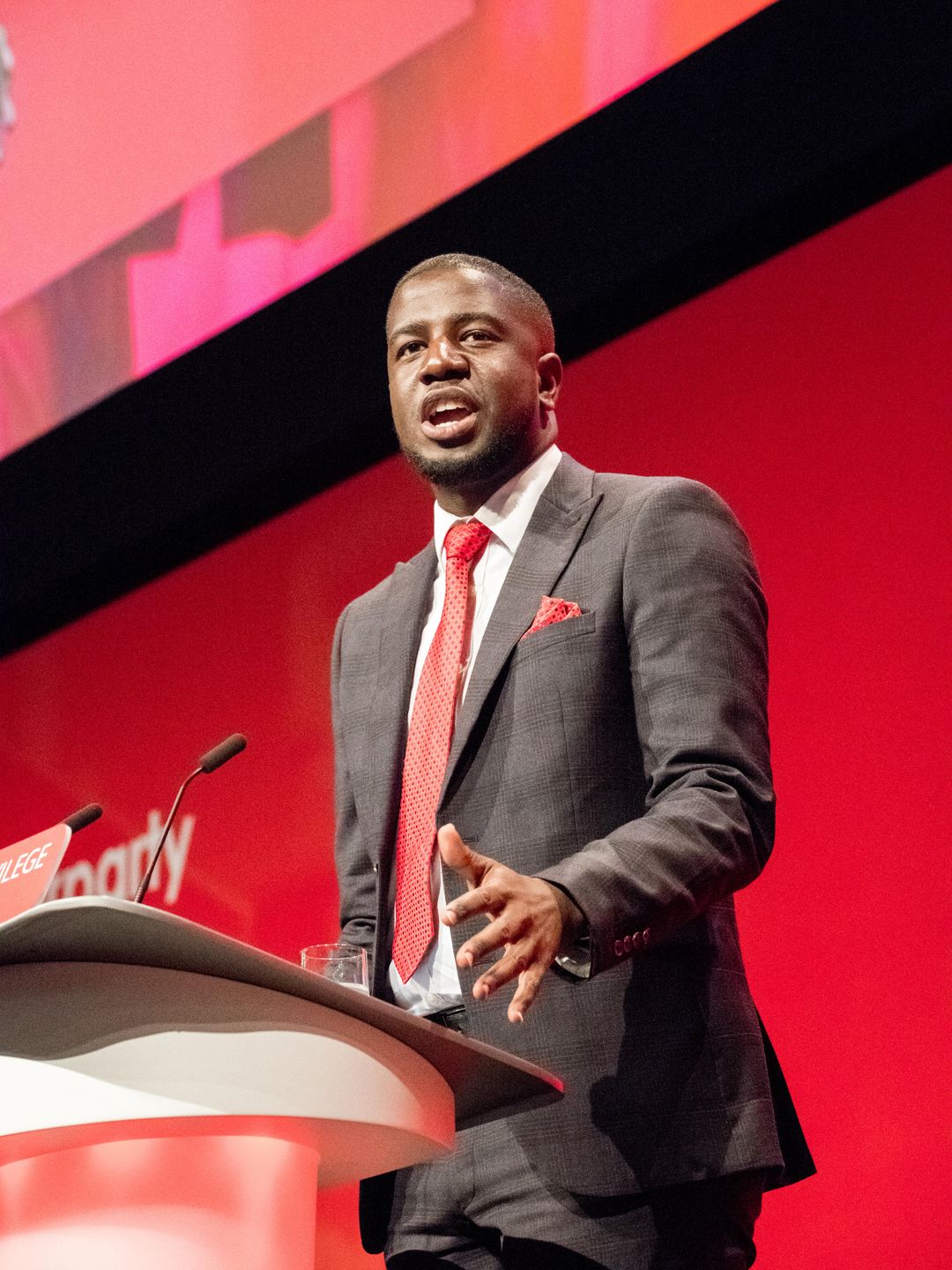 Jermain Jackson in a black suit and red tie addressing delegates of the Labour Party